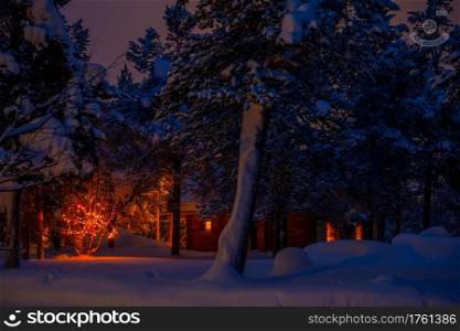 Wooden house in the night winter forest and Christmas garland. A lot of snow. Illuminated Cottage and Garland in a Nightly Snowy Forest