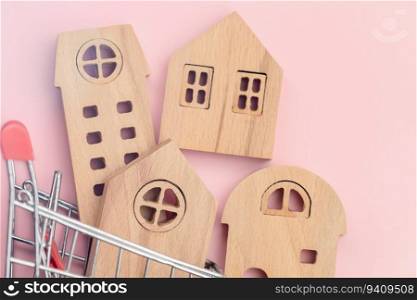 Wooden house model in the shopping cart on pink background for housing and property concept