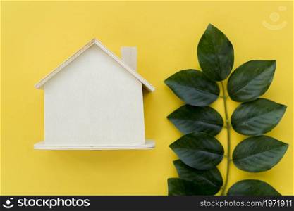 wooden house model near green leaves against yellow background. High resolution photo. wooden house model near green leaves against yellow background. High quality photo