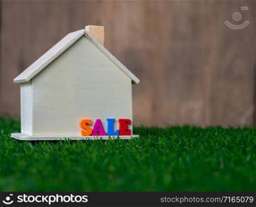 Wooden house model placed on a green lawn and colorful text sale on the house. Eco house concept