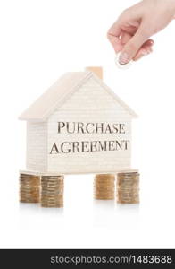 Wooden house model standing on coins and hand holding the coin with conceptual text. Purchase Agreement