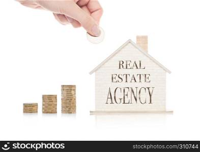 Wooden house model with coins next to it and hand holding the coin with conceptual text.Real Estate Agency