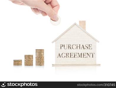 Wooden house model with coins next to it and hand holding the coin with conceptual text. Purchase Agreement