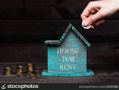 Wooden house model with coins next to it and hand holding the coin with conceptual text. House for rent