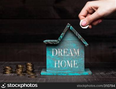Wooden house model with coins next to it and hand holding the coin with conceptual text. Dream Home