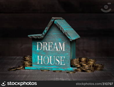 Wooden house model with coins next to it with conceptual text. Dream House