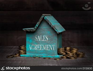 Wooden house model with coins next to it with conceptual text. Sales Agreement