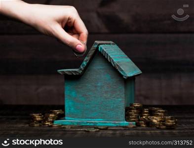 Wooden house model with coins next to it with for conceptual text and female hand puts coin