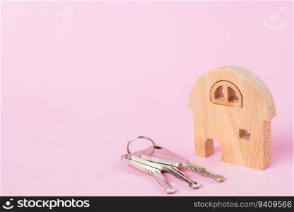 Wooden house model with keys on soft pink background for housing and property concept