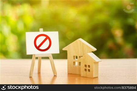 Wooden houses and an easel with a red prohibition sign NO. Inaccessibility and lack of housing, deficit. Seizure and freezing of assets by a bank, court. Illegal buildings, demolition elimination
