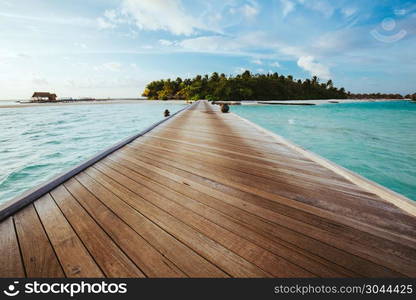 Wooden jetty on clear water leading to an island. Tropical vacation on Maldives. Jetty on sea leading to an island.