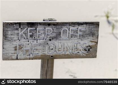 Wooden keep off sign and white sand dunes on the beach on a hot summer afternoon.