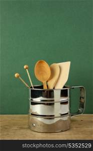 wooden kitchenware in metal jug on old wooden table over green background