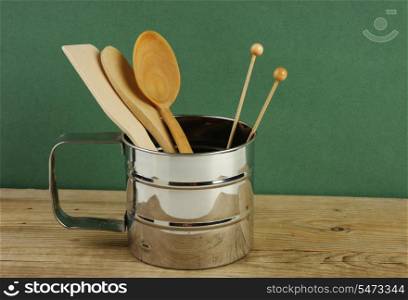 wooden kitchenware in metal jug on old wooden table over green background