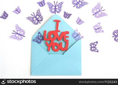"Wooden lettering "I love you" in a blue envelope and flying purple paper butterflies."
