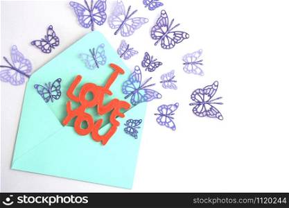 "Wooden lettering "I love you" in a blue envelope and flying purple paper butterflies."