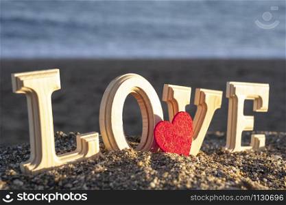 wooden letters forming the word love with a red heart on the seashore. concept of lovers