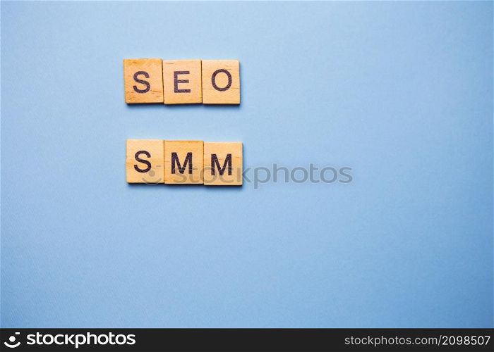 Wooden letters SEO and SMM are printed on a light blue background. Wooden letters SEO and SMM are printed on a light blue background.