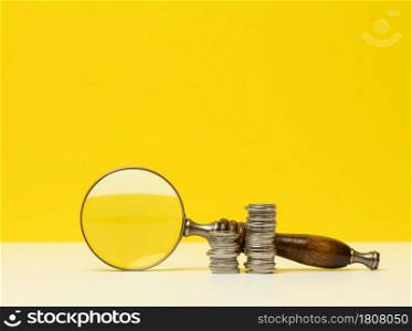 wooden magnifier and white coins on the table. Income growth concept, high percentage of investment. Search for new sources of income, subsidy