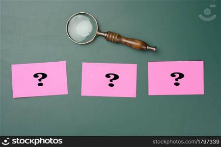 wooden magnifying glass and white chalk drawn question marks on a green chalk board. The concept of finding solutions, true or false. Answers on questions