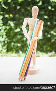 Wooden manikin carrying colour pencil on artist work table, stock photo
