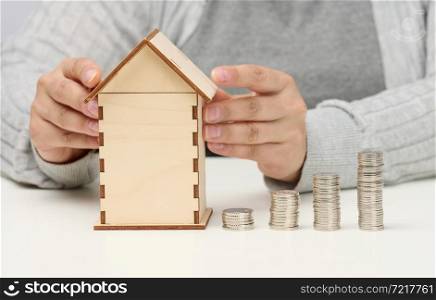 wooden model of a house, a stack of coins. The man sits at the table. Higher property prices, higher rents and higher mortgage interest rates