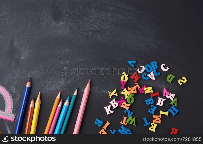 wooden multi-colored pencils, letters on a black wooden board, concept of learning, back to school, copy space
