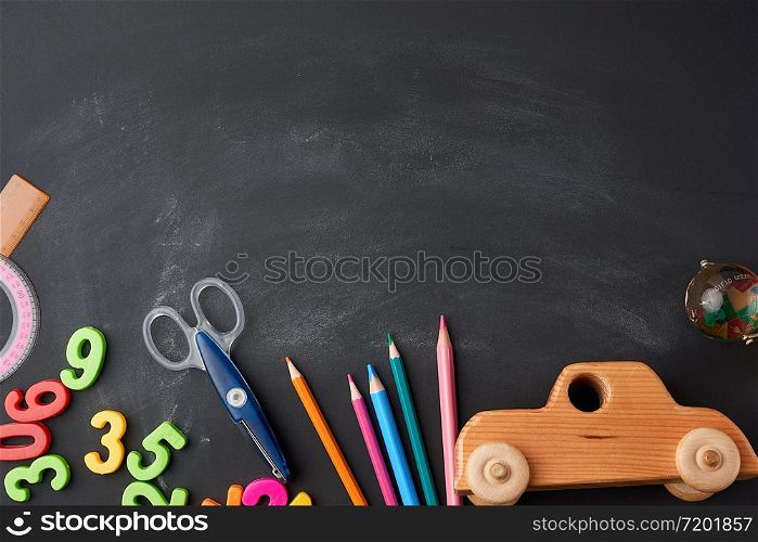 wooden multi-colored pencils, plastic numbers, scissors, wooden toy car on a black background, concept back to school, copy space