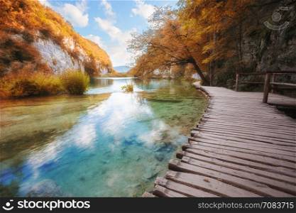 Wooden path across lake in sunny autumn park