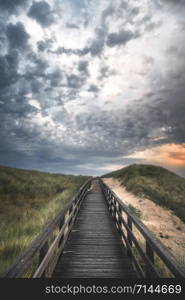 Wooden path through high grass hill, sandy dune, on Sylt island, at North Sea, Germany, at sunset. Bridge over dunes, a protected area in northern.