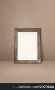 Wooden picture frame leaning on a beige wall. Blank mockup template. Wooden picture frame leaning on a beige wall