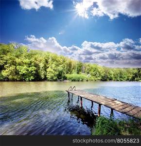 Wooden pier in the small lake under blue sunny sky. Wooden pier in the small lake