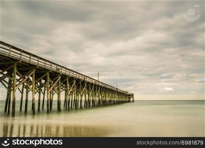wooden pier leads out into a calm ocean on a summer day