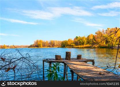 Wooden pier on river at sunny autumn day. Autumn and wooden pier