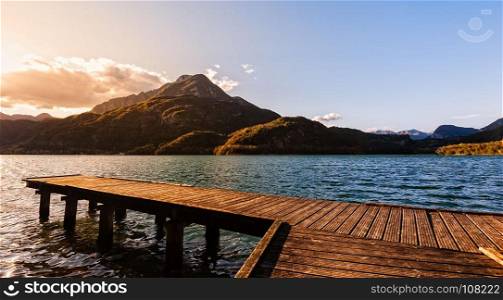 Wooden pier on the lake at sunset with mountains in the background.