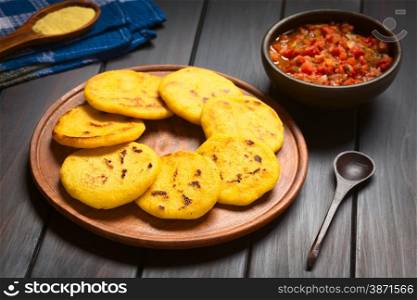 Wooden plate of arepas with Colombian hogao sauce (tomato and onion cooked) in the back. Arepas are made of yellow or white corn meal and are traditionally eaten in Colombia and Venezuela (Selective Focus, Focus on the first arepas)