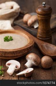 Wooden plate of creamy chestnut champignon mushroom soup with wooden spoon, pepper and kitchen cloth on wooden board.