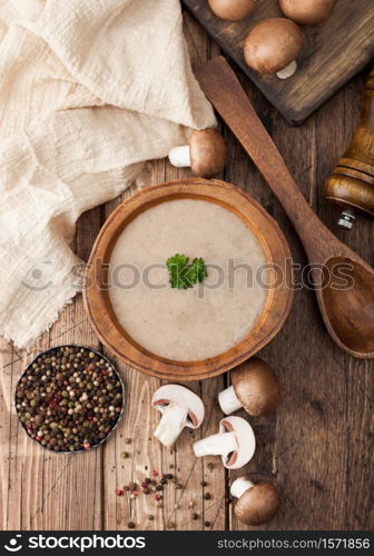 Wooden plate of creamy chestnut champignon mushroom soup with wooden spoon, pepper and kitchen cloth on wooden board.