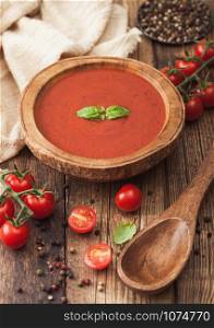 Wooden plate of creamy tomato soup with wooden spoon, pepper and kitchen cloth on wooden board. with raw tomatoes.