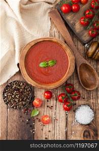 Wooden plate of creamy tomato soup with wooden spoon, pepper and kitchen cloth on wooden board. with raw tomatoes. Top view.