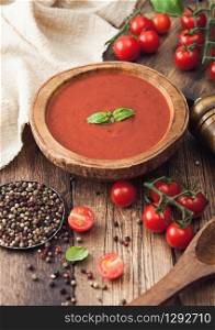 Wooden plate of creamy tomato soup with wooden spoon, pepper and kitchen cloth on wooden board. with raw tomatoes. Top view.