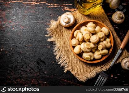 Wooden plate on burlap with pickled mushrooms. Against a dark background. High quality photo. Wooden plate on burlap with pickled mushrooms.