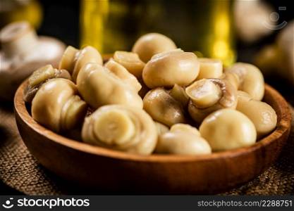 Wooden plate on burlap with pickled mushrooms. Against a dark background. High quality photo. Wooden plate on burlap with pickled mushrooms.