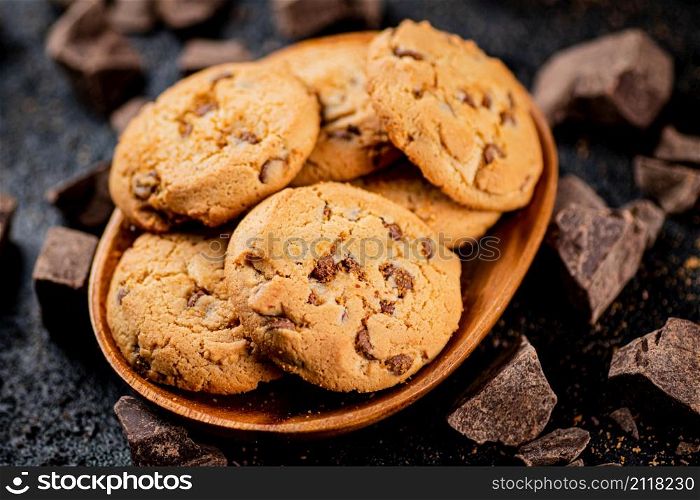 Wooden plate with cookies and pieces of milk chocolate. On a black background. High quality photo. Wooden plate with cookies and pieces of milk chocolate.