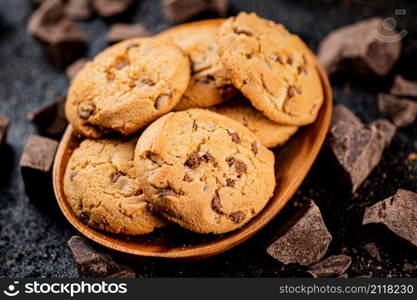 Wooden plate with cookies and pieces of milk chocolate. On a black background. High quality photo. Wooden plate with cookies and pieces of milk chocolate.