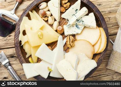 Wooden plate with different kinds of cheese on table. Set of sliced cheeses