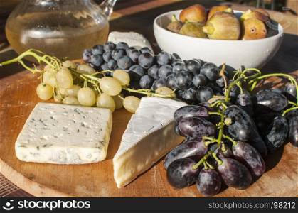 Wooden plateau with fresh grapes figs and types of cheese closeup as homefood background
