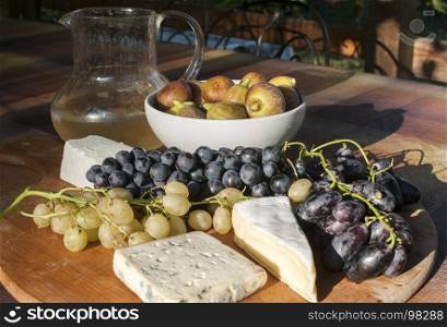 Wooden plateau with fresh grapes figs and types of cheese closeup as homefood background