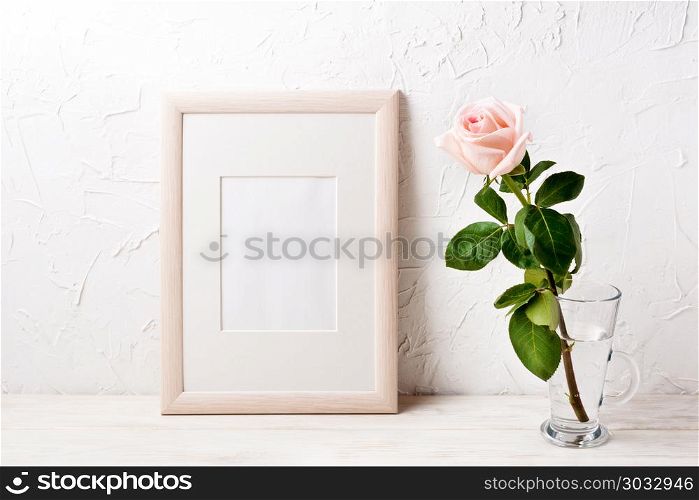 Wooden poster frame mockup with pale pink rose in glass mug. Empty frame mock up for presentation design. Template framing for modern art.. Wooden frame mockup with pink rose