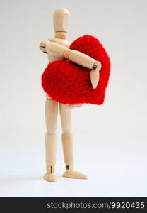 Wooden puppet standing and holding a red heart on the white screen background. Wooden puppet holding the heart with love and care.